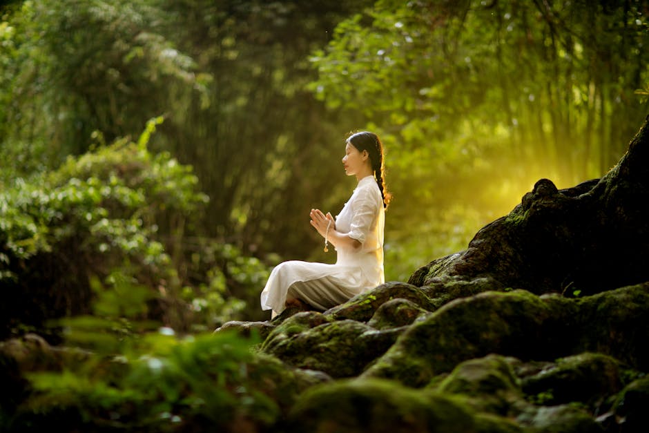 Serene woman in a seated yoga pose with hands in prayer, against a calm outdoor backdrop.